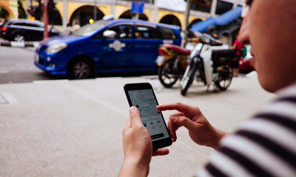 Man stands on sidewalk with ride-hailing app on phone