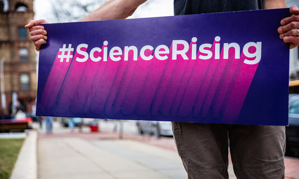 Man holding Science Rising sign on city street