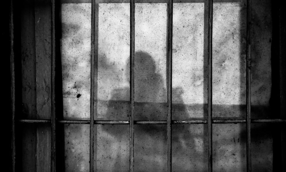 Image of prison bars with a person's shadow behind them.