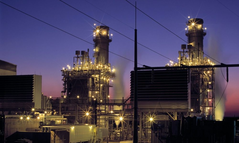 the lights of a power plant shine against a purple dusk