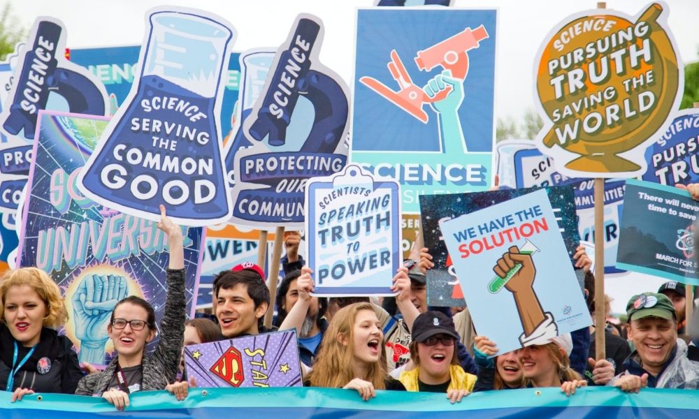 a group of science activists marches for science, holding signs that say "Scientists speaking truth to power," and "science serving the common good"