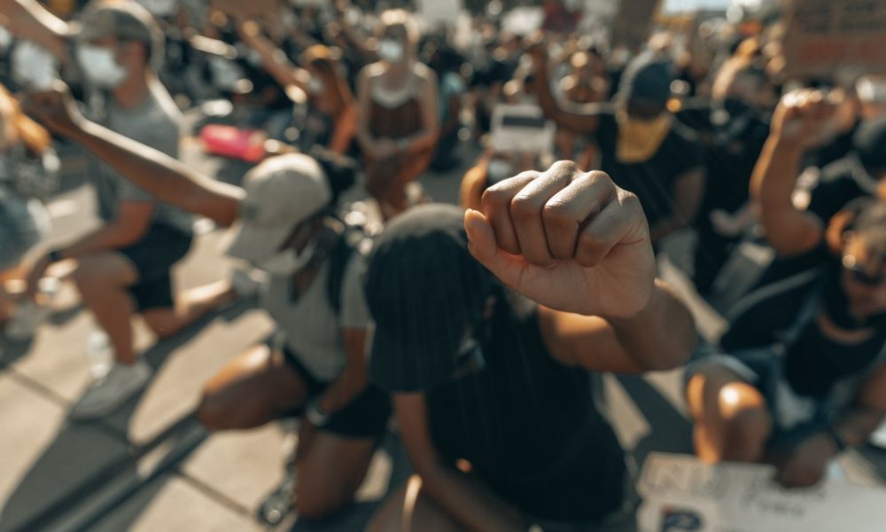 Two people in the foreground of a group of protestors raise their fists in solidarity for George Floyd