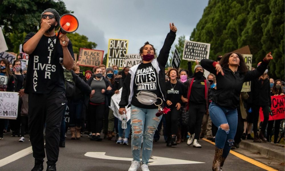 a group of young-looking people wearing Black Lives Matter tee-shirts and holding Black Lives Matter signs march peacefully down a street