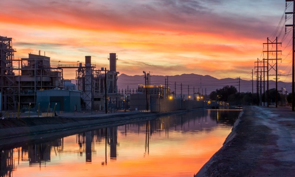 Sun either rises or sets above or below a complicated-looking facility on a river in Tempe, Arizona