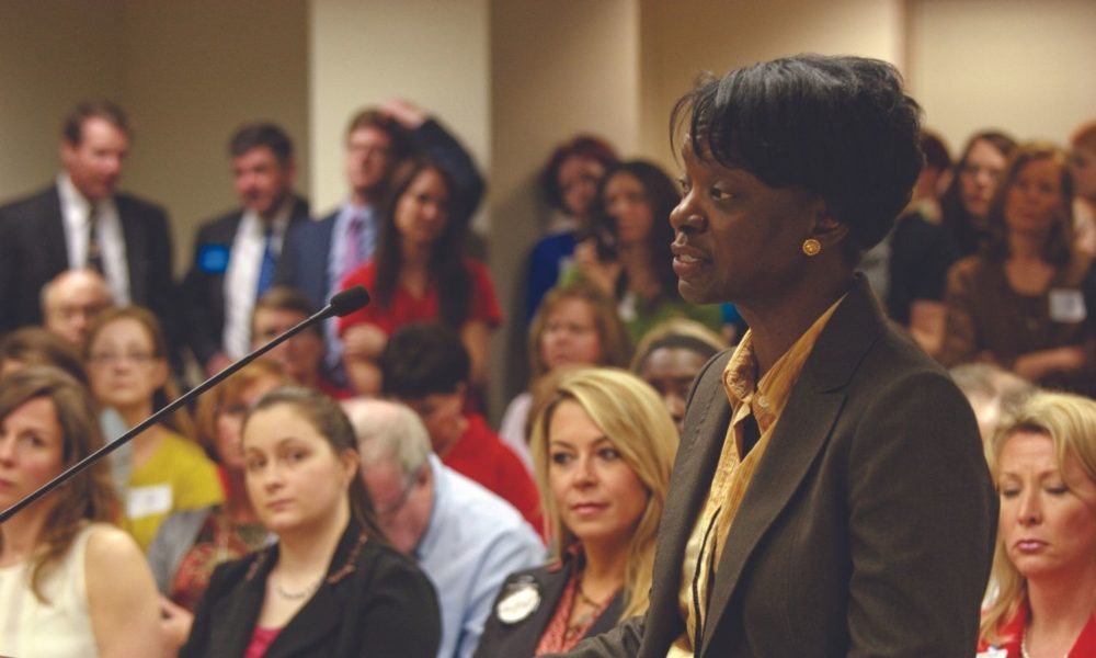 a woman speaks into a microphone at what appears to be a community meeting