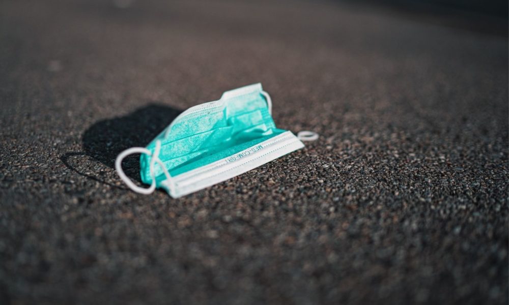 a discarded surgical mask lies on asphalt