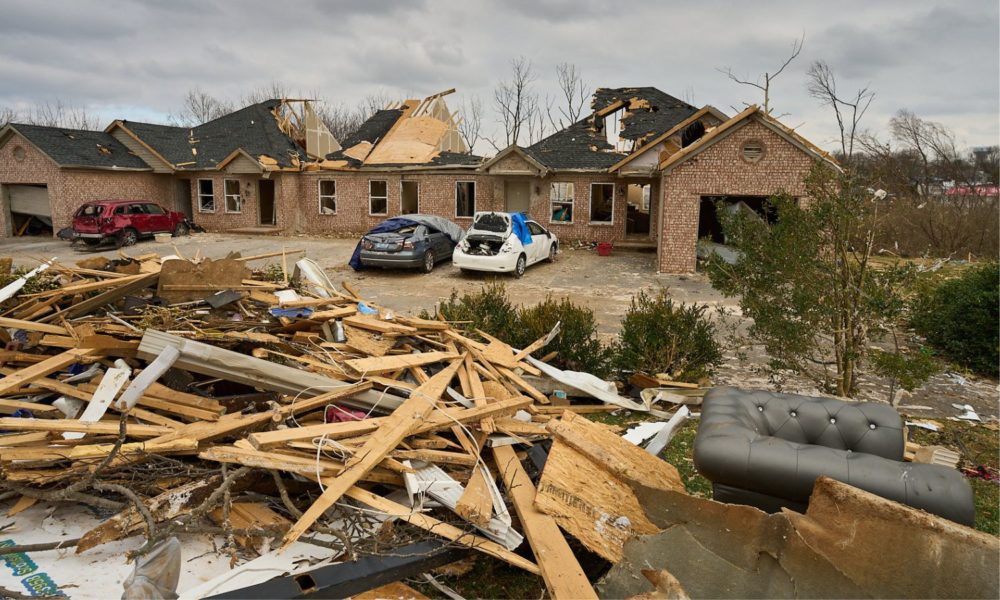 A scene of destruction in Bowling Green, KY, with a pile of rubble including a couch in the foreground, and a destroyed home in the background