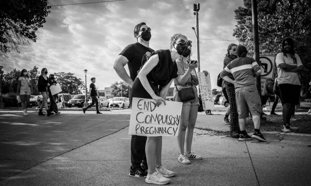 A group of people at a Des Moines, Iowa, protest against Roe v. Wade being overturned by the Supreme Court. One person holds a sign reading "end compulsory pregnancy."