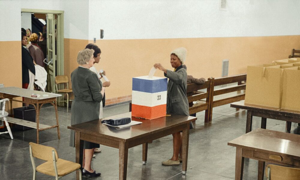 A young Black woman hands in her ballot at a polling station in 1964, in Washington, DC