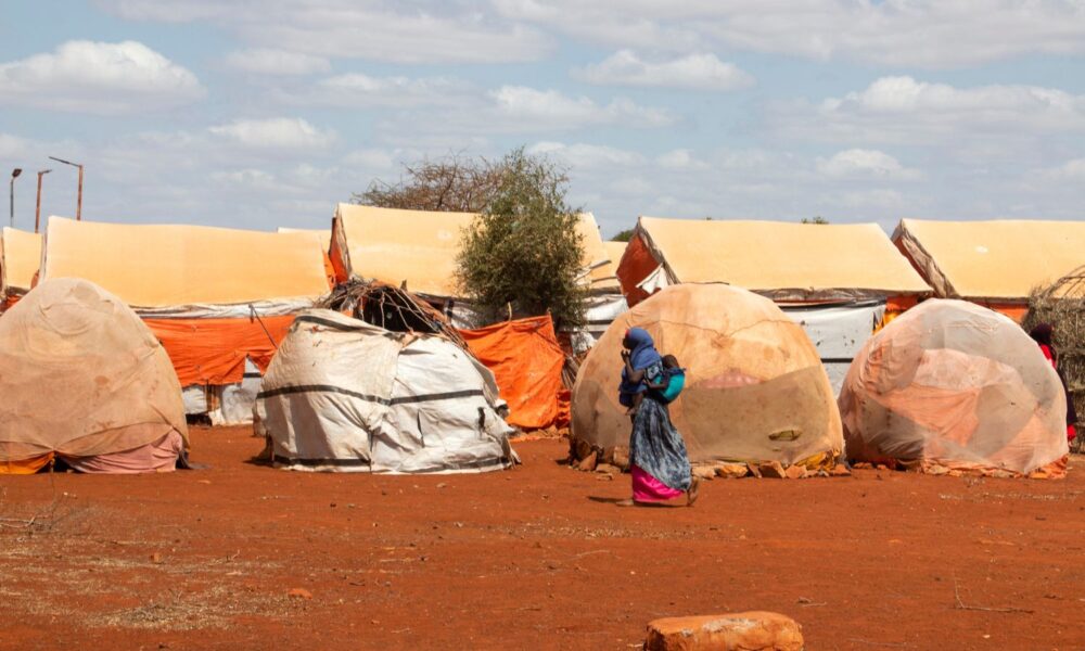 A woman with a child in a carrier on her back walks through a refugee camp in Somalia, where catastrophic drought has created over a million refugees