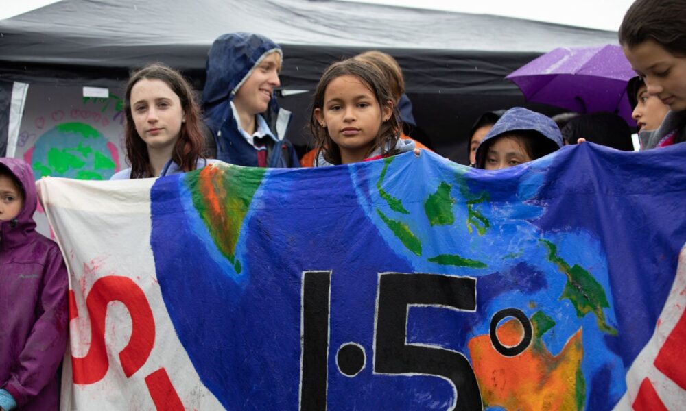 A few children hold up a painted banner with the Earth pictured, and the numbers 1.5, indicating the limit of global warming temperature increase for a viable future