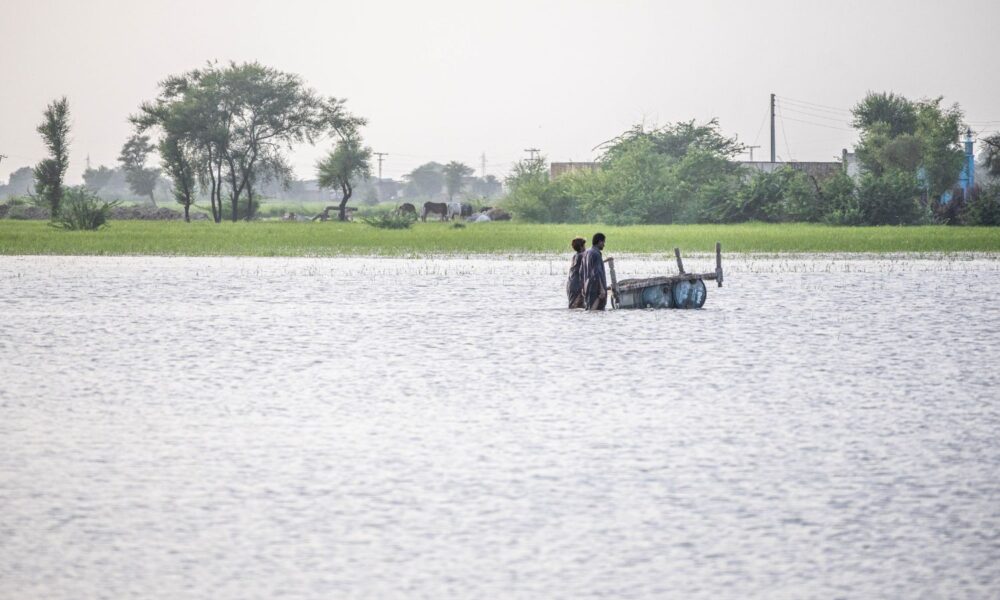 Two people push a cart through a river in Balochistan, Pakistan, after intense flooding in 2022