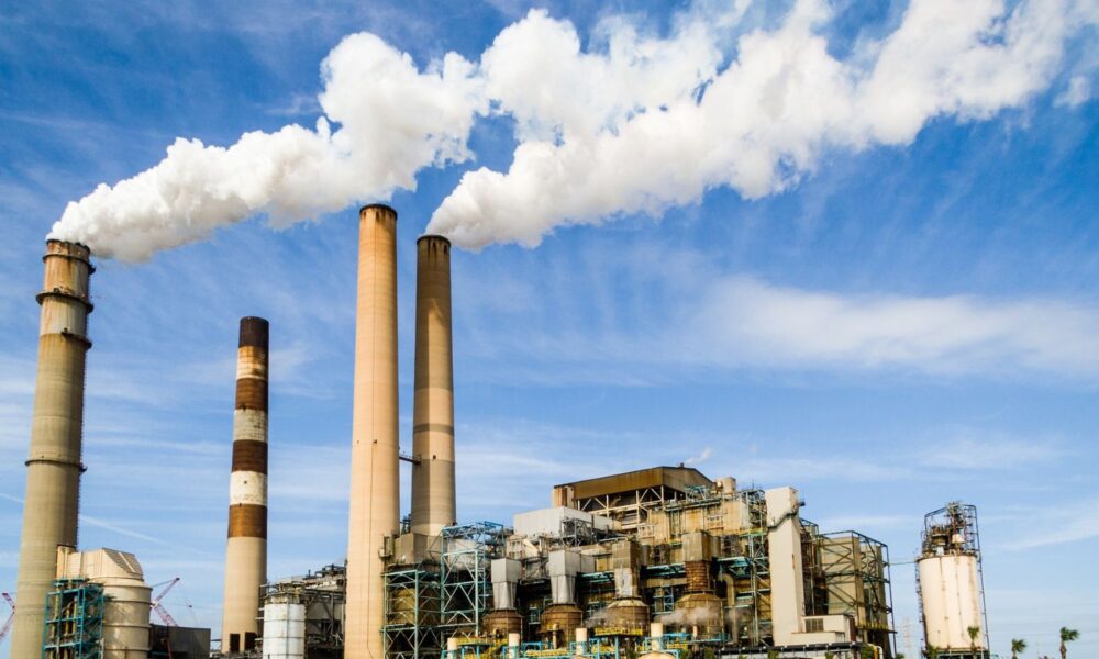 Against a bright blue sky, a power plant emits clouds of white smoke