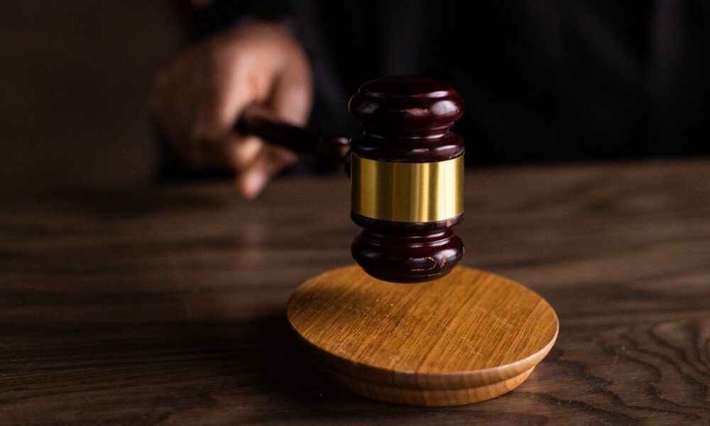 photo of a gavel being tapped on a courtroom desk; the judge's hand holding the gavel can barely be seen in the dark background