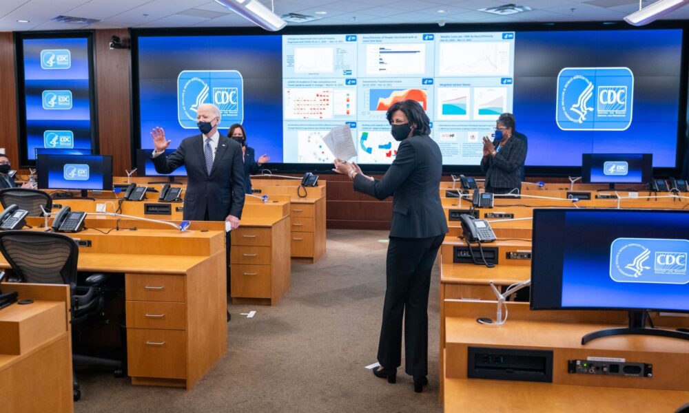 President Joe Biden, joined by Vice President Kamala Harris and former Director of the Centers for Disease Control Dr. Rochelle Walensky, talks with CDC staff during a briefing in 2021, at the CDC headquarters in Atlanta. Everyone is wearing face masks.