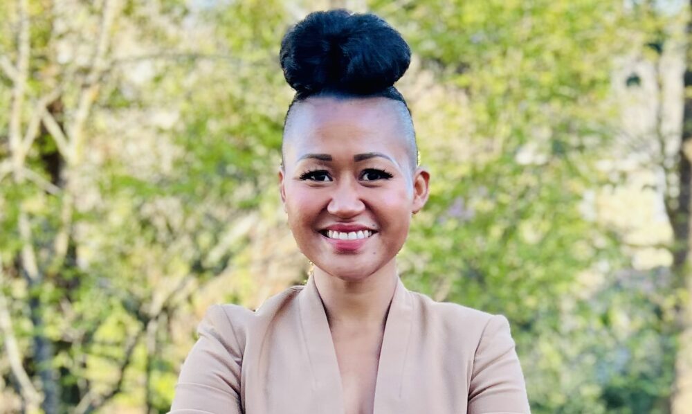 photo of Dania Davy smiling for the camera, with woods and filtered sunlight in the background