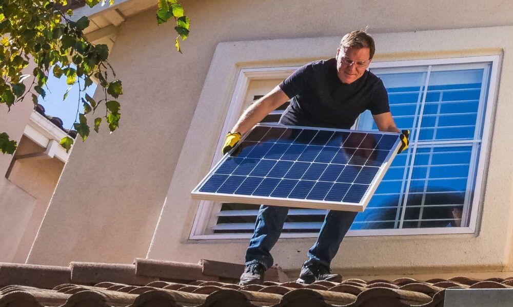 man standing on roof while holding a solar panel