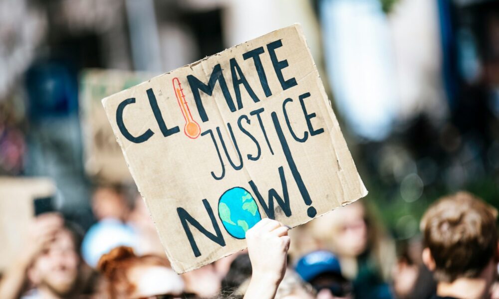 A cardboard sign held aloft at a protest reads CLIMATE JUSTICE NOW