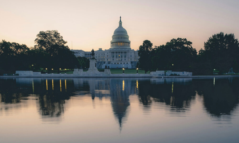 photo of the US Capitol at dusk, with its silhouette and streetlights reflected on water in the foreground