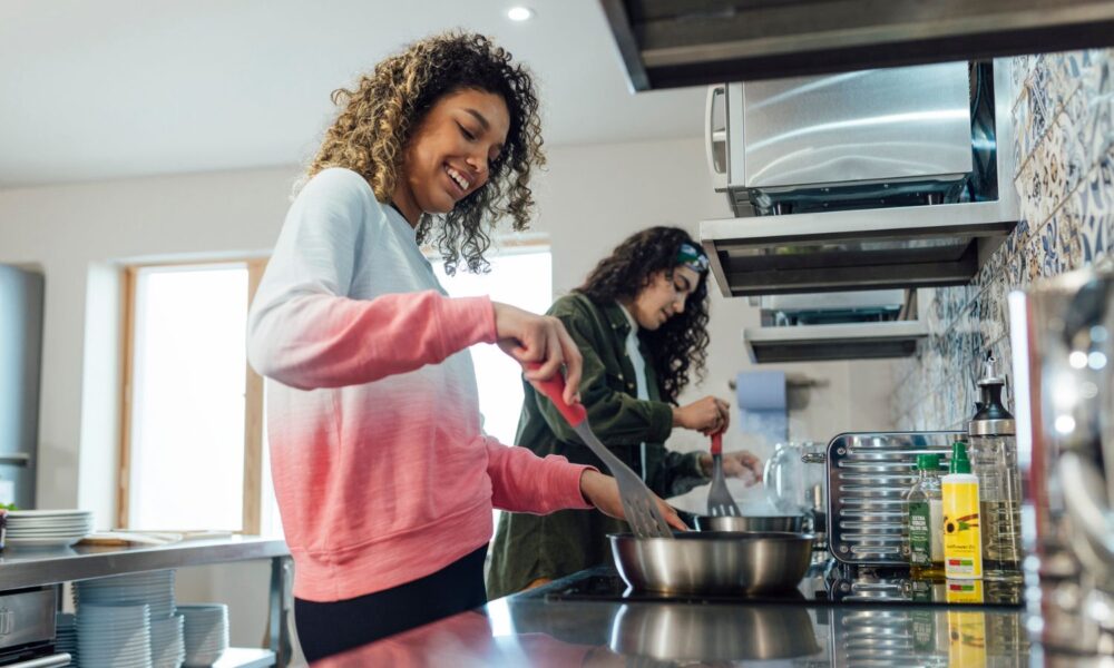 Two women cook in a kitchen on an induction stove.