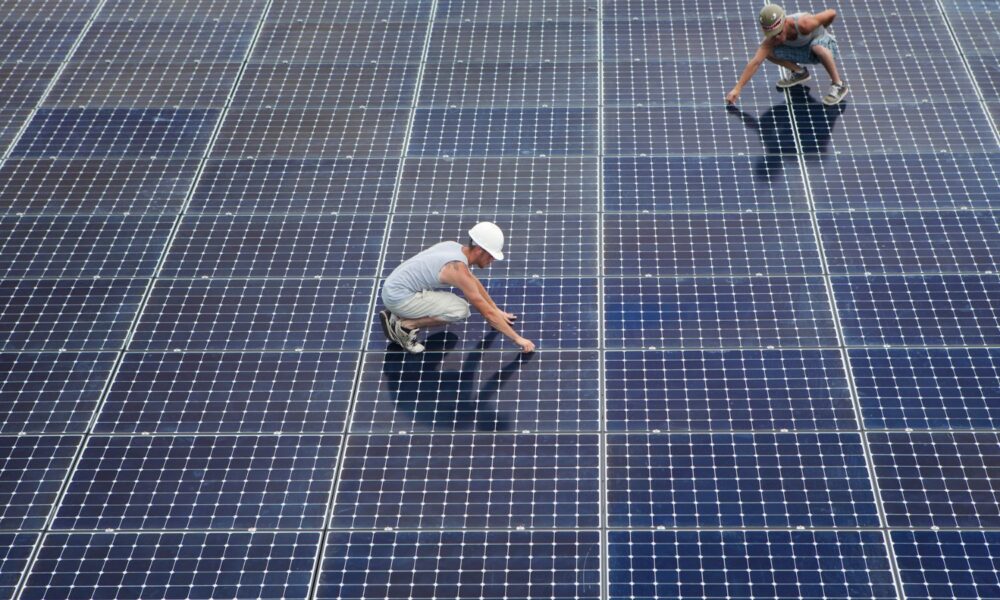 Two men installing solar panels on rooftop.