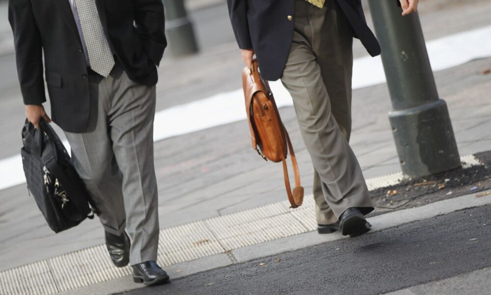 White men in suits carrying briefcases cross a street.