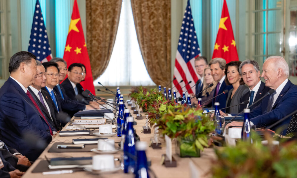 photo of a 2023 meeting between the US and China; President Xi Jinping and members of his staff sit on the left side of the table and President Joe Biden and members of his staff sit on the right side; flags of both countries are in the background