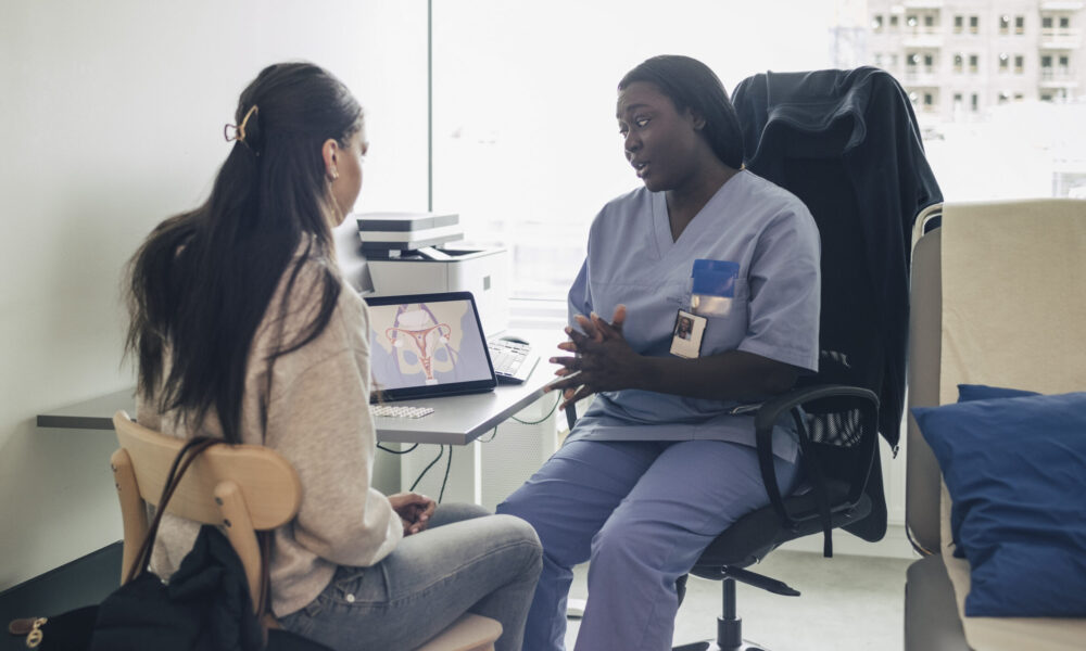 A woman in medical scrubs sits across from another woman