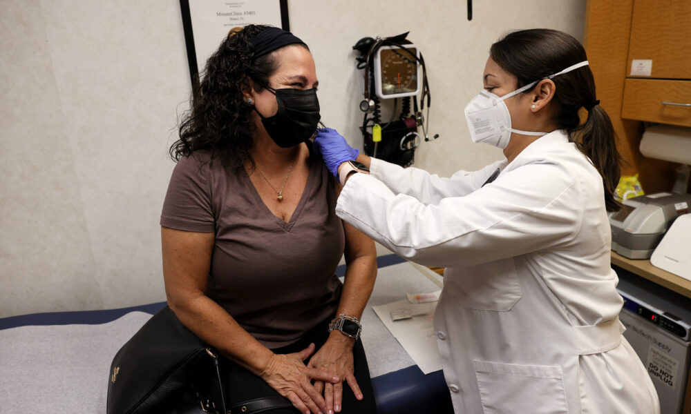 a woman in a mask and lab coat gives a woman in a mask a shot in a medical office