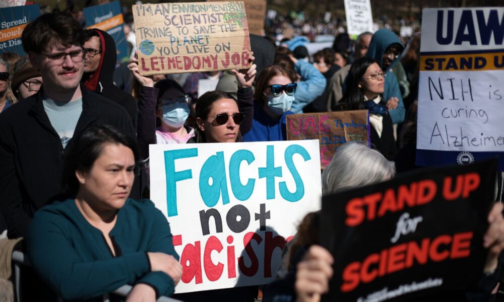 People carrying signs, one of which reads "facts not fascism," and another "I'm an environmental scientist trying to save the planet you live on. Let me do my job" at the Stand Up for Science 2025 rally at the Lincoln Memorial on March 7, 2025 in Washington, DC.