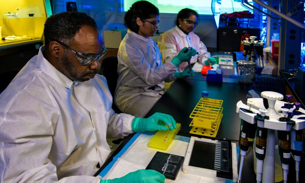 three scientists in goggles and lab coats conduct experiments.