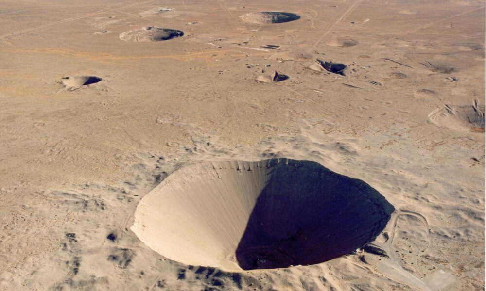 aerial photo of the large Sedan Crater created by an underground nuclear blast the Nevada Test Site; several smaller craters are in the desert floor in the background