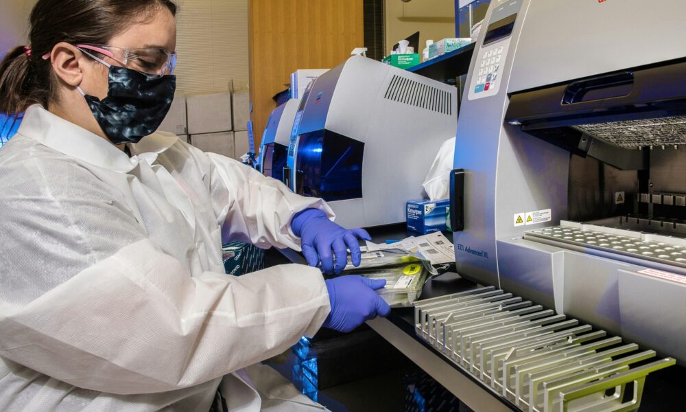 a scientist in a lab coat, mask, and goggles sorting samples in a lab