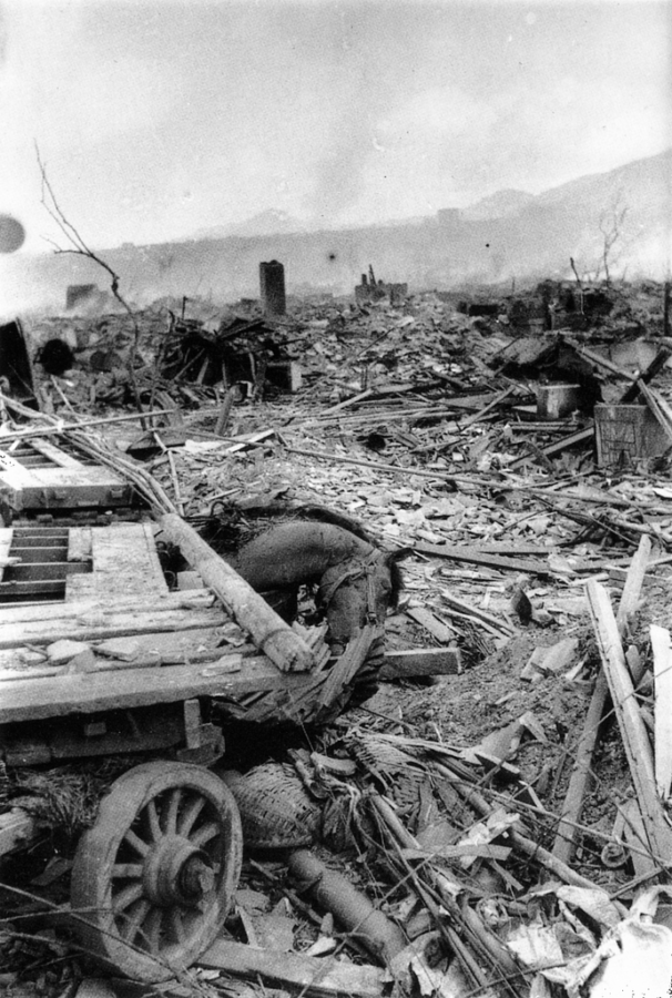 Black and white photograph showing rubble and debris in the aftermath of the bombing of Nagasaki, Japan. A horse is seen, dead, on the ground near its cart.
