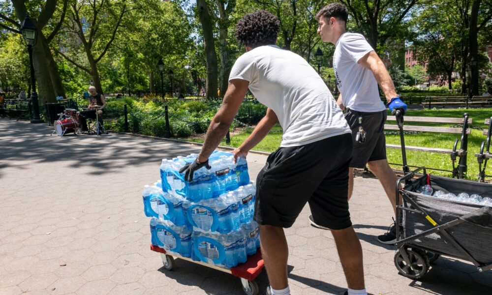 Two young people move a pallet of water bottles through a park in NYC during a heat wave in 2025.