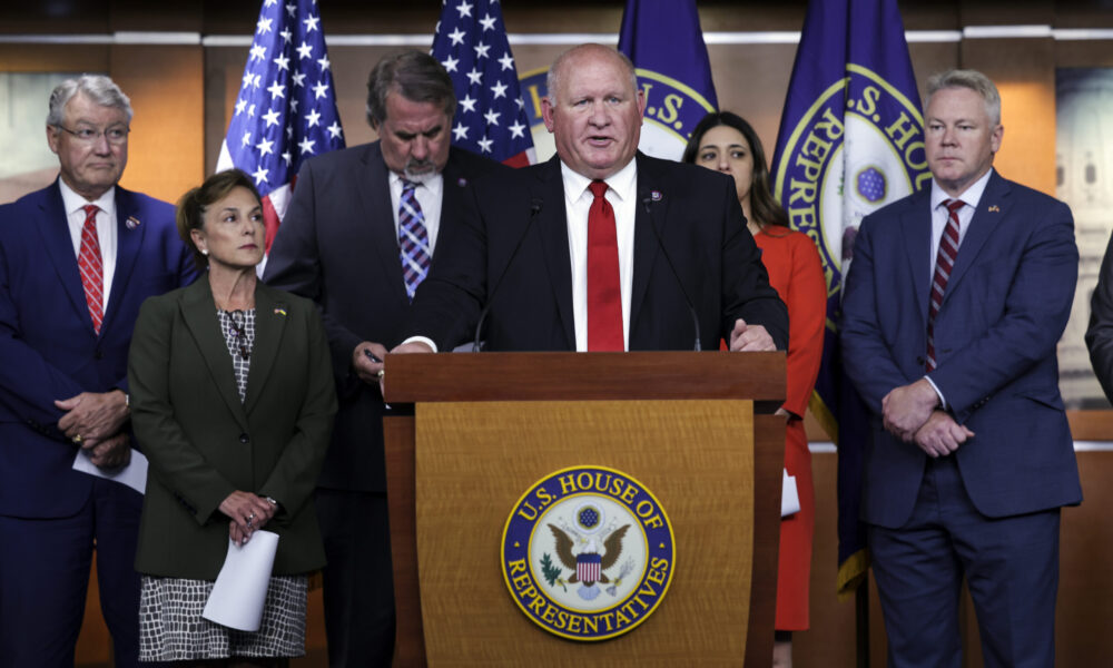 photo of House Agriculture Committee Chairman G.T. Thompson speaking from a podium with the seal of the House of Representatives; behind him are other Republican members of the committee and several flags