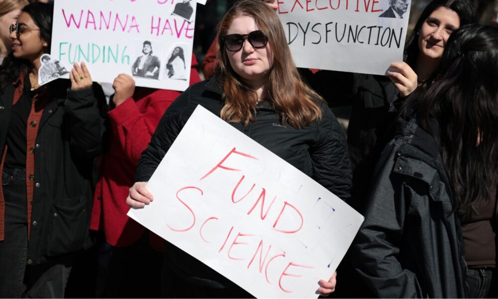 A younger person holds a sign that reads FUND SCIENCE at a national Stand up for Science rally in 2025.