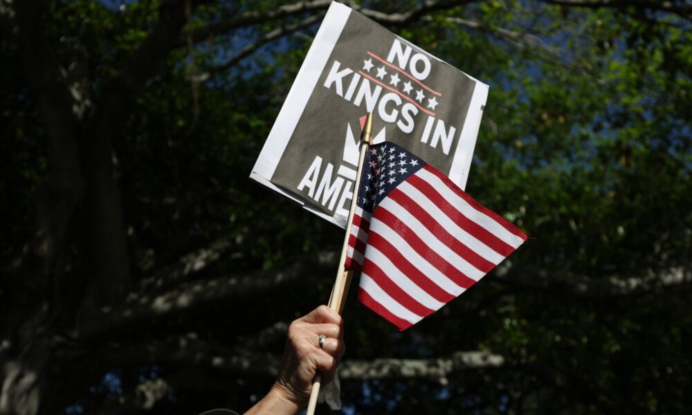A hand holding a US flag and a "No Kings" protest sign.