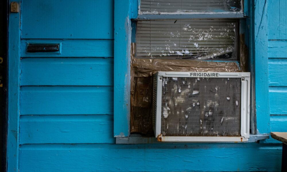 An old air conditioning unit in a window of a blue house.