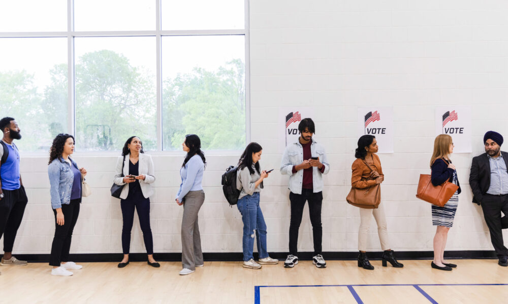 a diverse group of 9 people standing in line waiting to vote