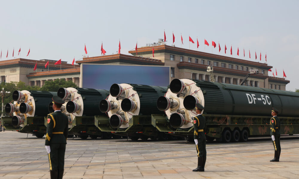 photo of four Chinese nuclear ICBMs on display during the country's 2025 Victory Day parade; soldiers stand guard in the foreground and a large building topped by many Chinese flags is in the background