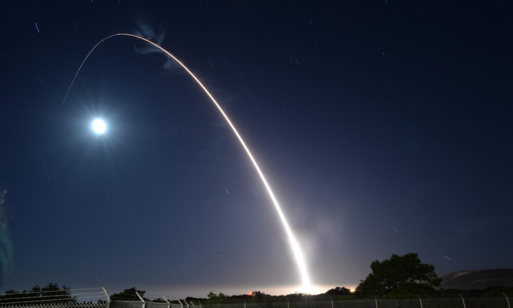 photo of a nighttime nuclear ICBM test launch; amid the darkness, the missile appears to arc up and over the moon