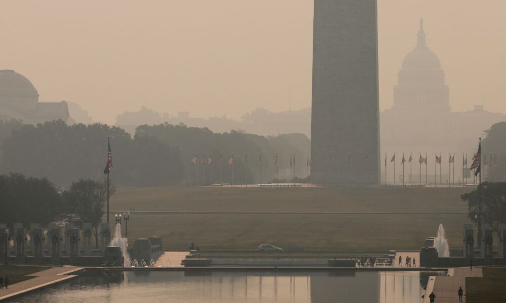 The sky and air in front of the US Capitol building are hazy and filled with smoke from wildfires, as people walk by
