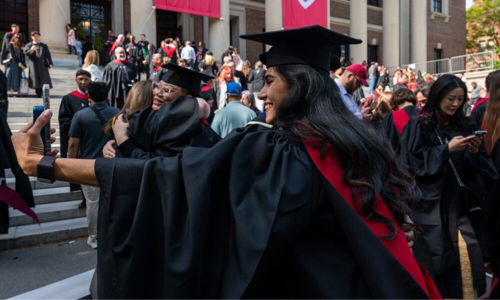 A student dressed in cap and gown takes a selfie at a commencement ceremony this spring