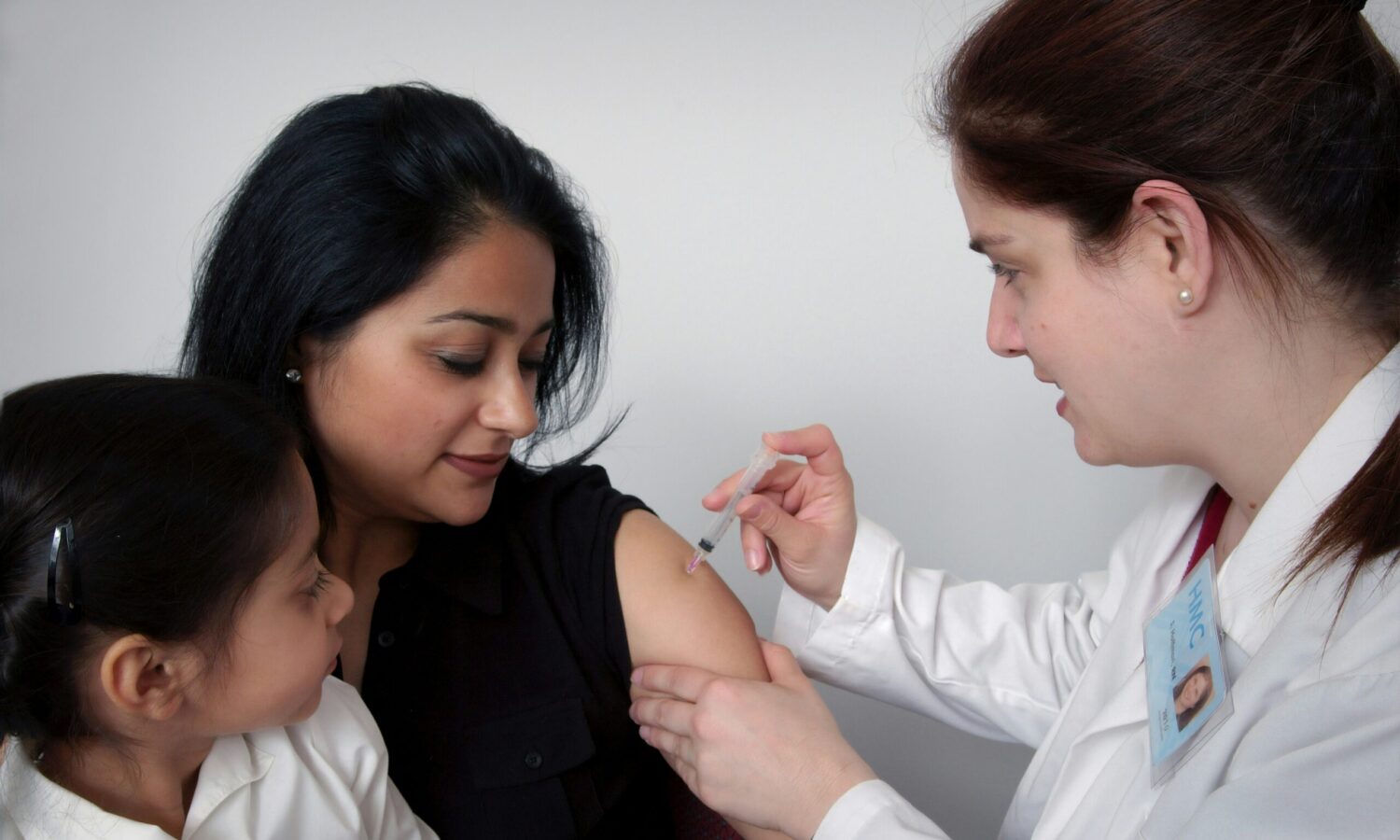 a woman holds a small child while another woman gives her an injection