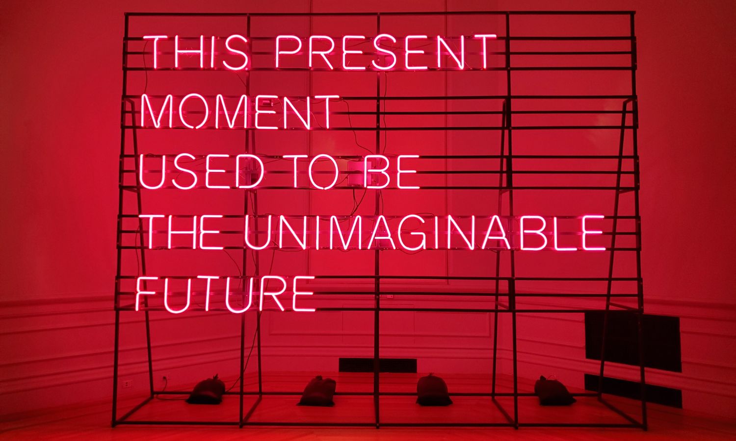 A neon light installation by artist Alicia Eggert in the Smithsonian Institute reads in hot pink lettering: this present moment used to be the unimaginable future.