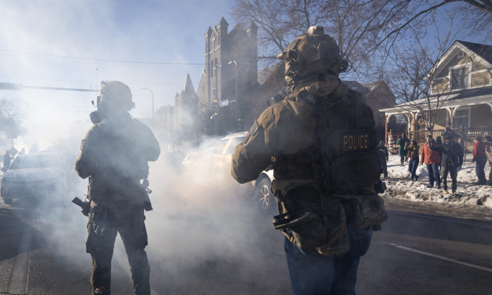 two armed federal agents standing in a cloud of tear gas on a suburban street