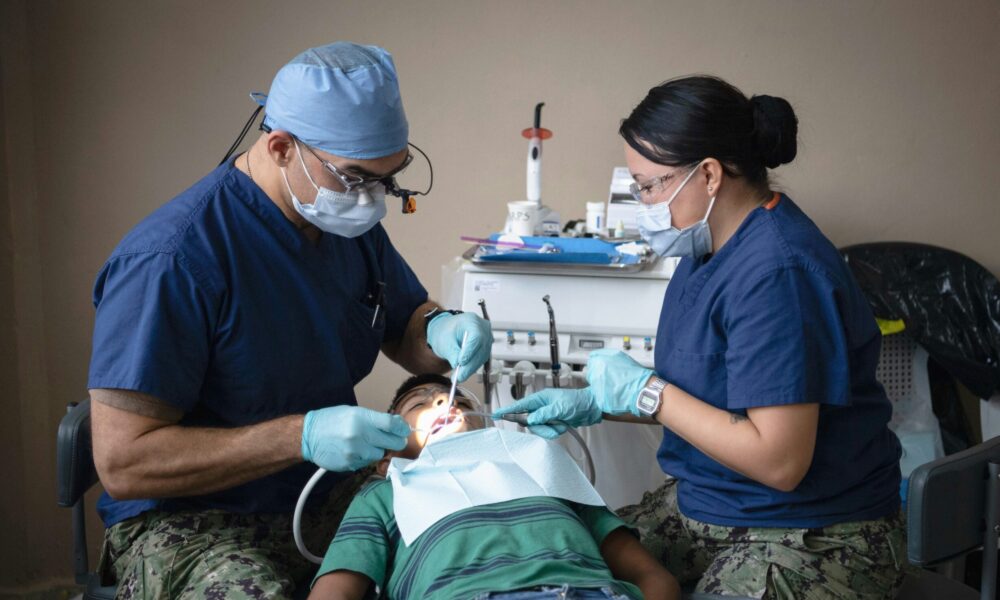 a child in a dentist's chair having their teeth examined by two people in blue scrubs