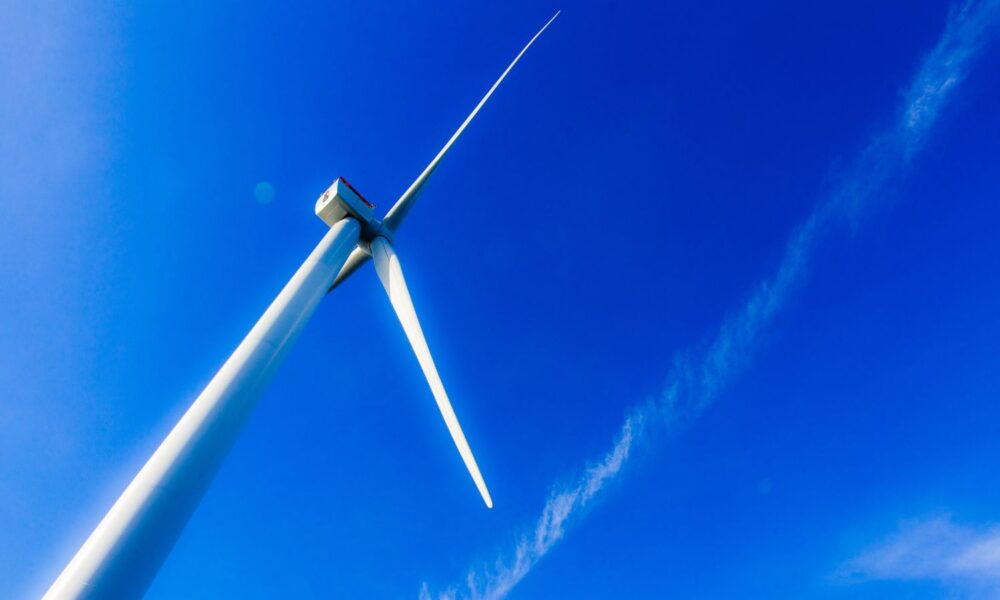 A wind turbine from the South Fork offshore wind farm on the East Coast glows brilliantly in the sun, set against a bright blue sky.