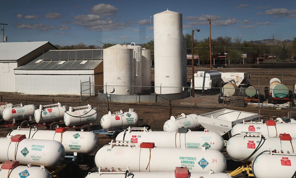 photo of numerous white storage tanks labeled "Anhydrous Ammonia: Inhalation Hazard" in the foreground; a warehouse and white silos are in the background